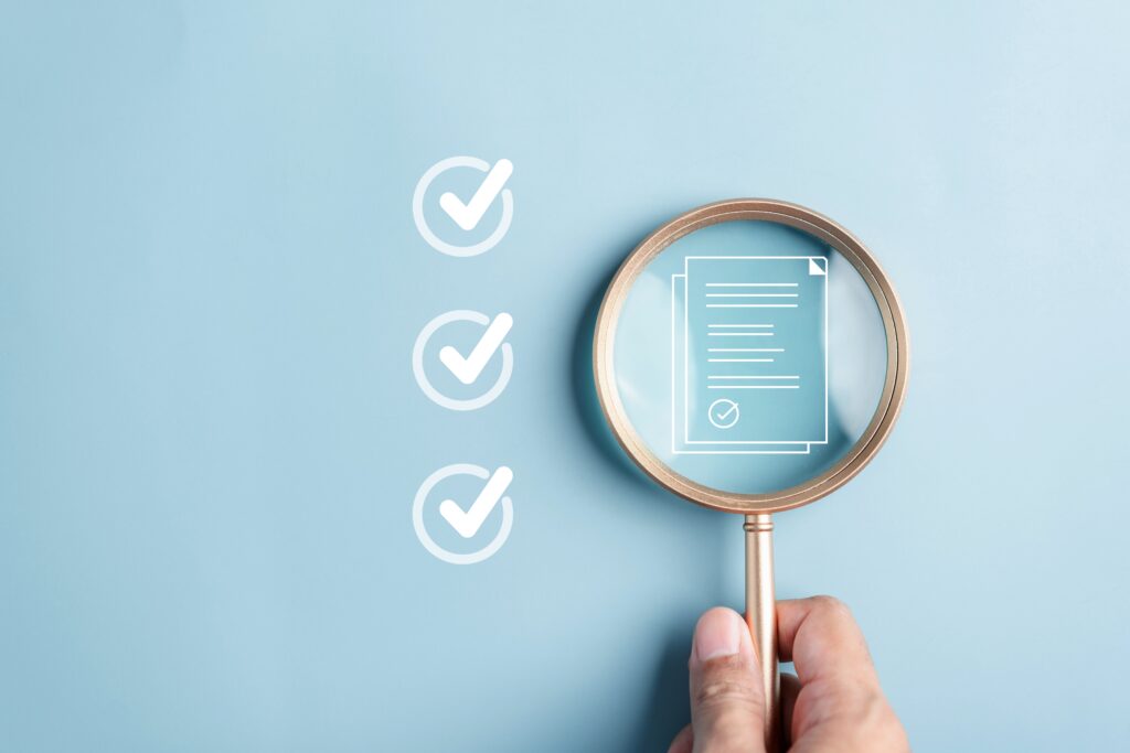 A hand holds a magnifying glass over a digital document icon next to three checkmarks on a light blue background.