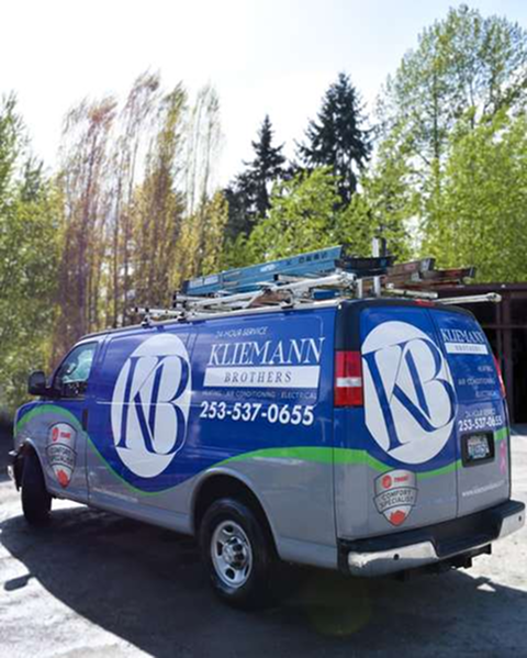 A Kleemann Brothers service van with a blue and white logo, ladders on the roof, parked outdoors near trees.