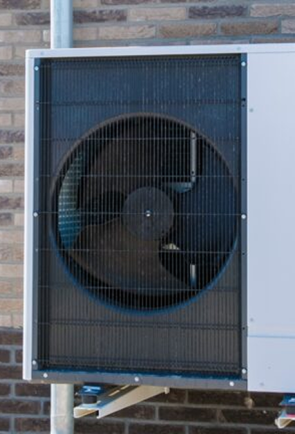 Outdoor unit of an air conditioning system with a visible large fan, mounted against a brick wall.