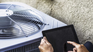 Person using a tablet near an outdoor hvac unit against a textured wall.